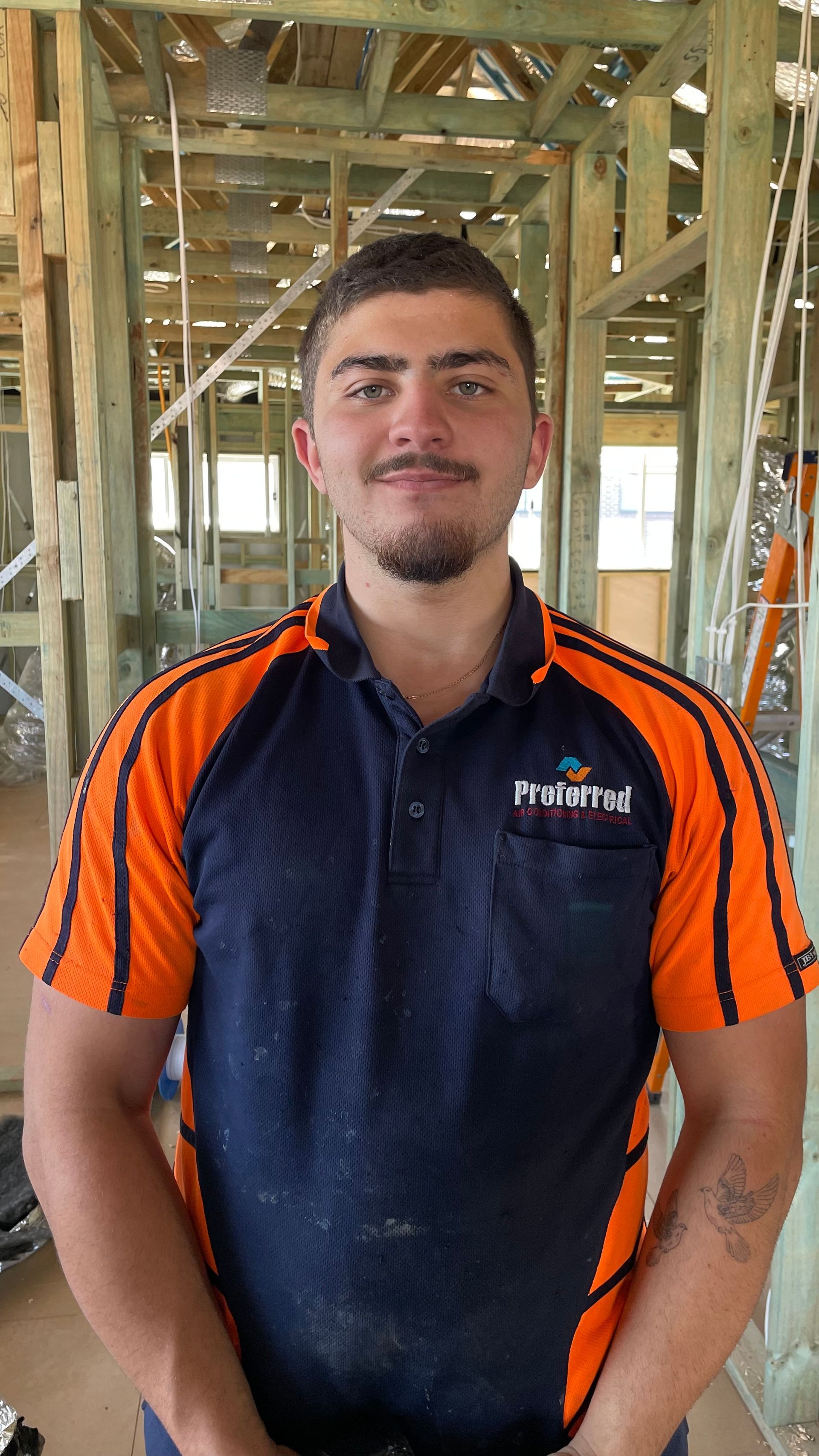 A man in an orange and blue shirt is standing in a building under construction.