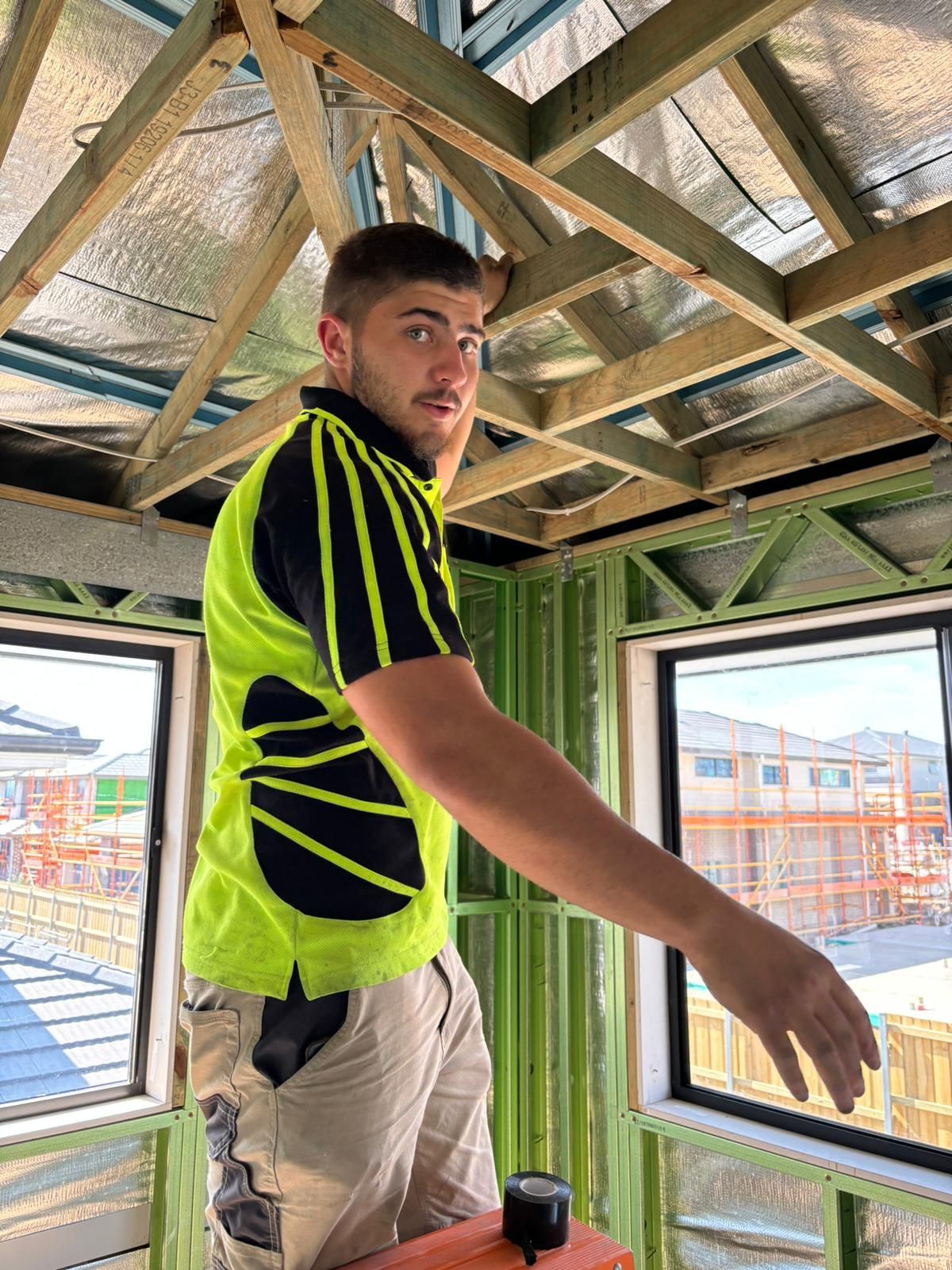 A man in a yellow and black shirt is standing in a room under construction.