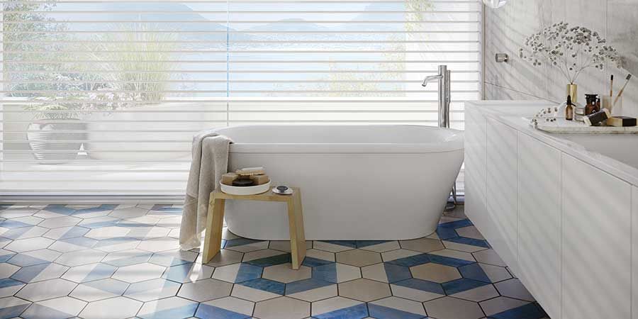 blue and beige tile floor in the main bathroom with white sheer shades on large windows 