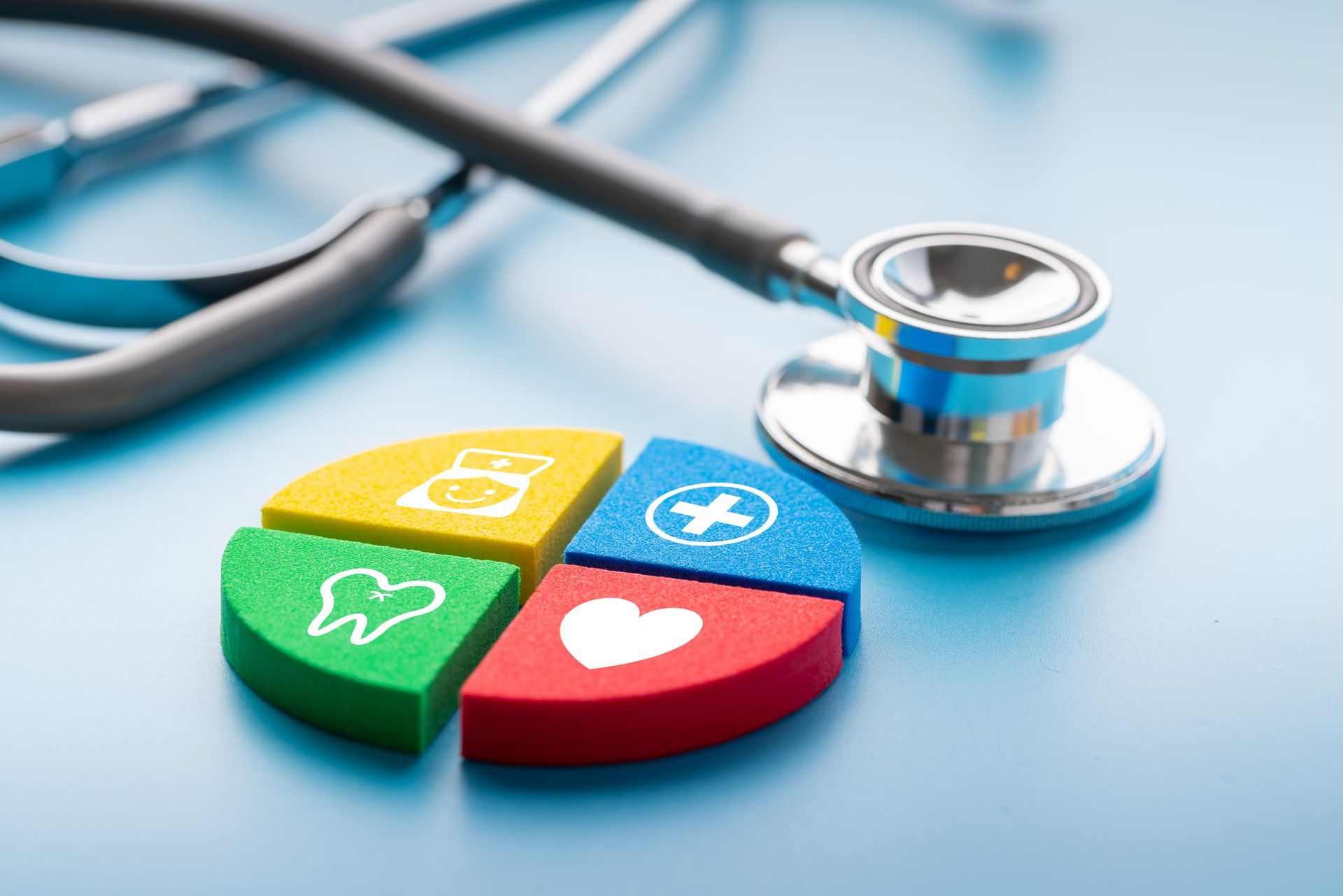 Stethoscope over a colorful pie chart with health icons, on a blue surface, representing healthcare options.