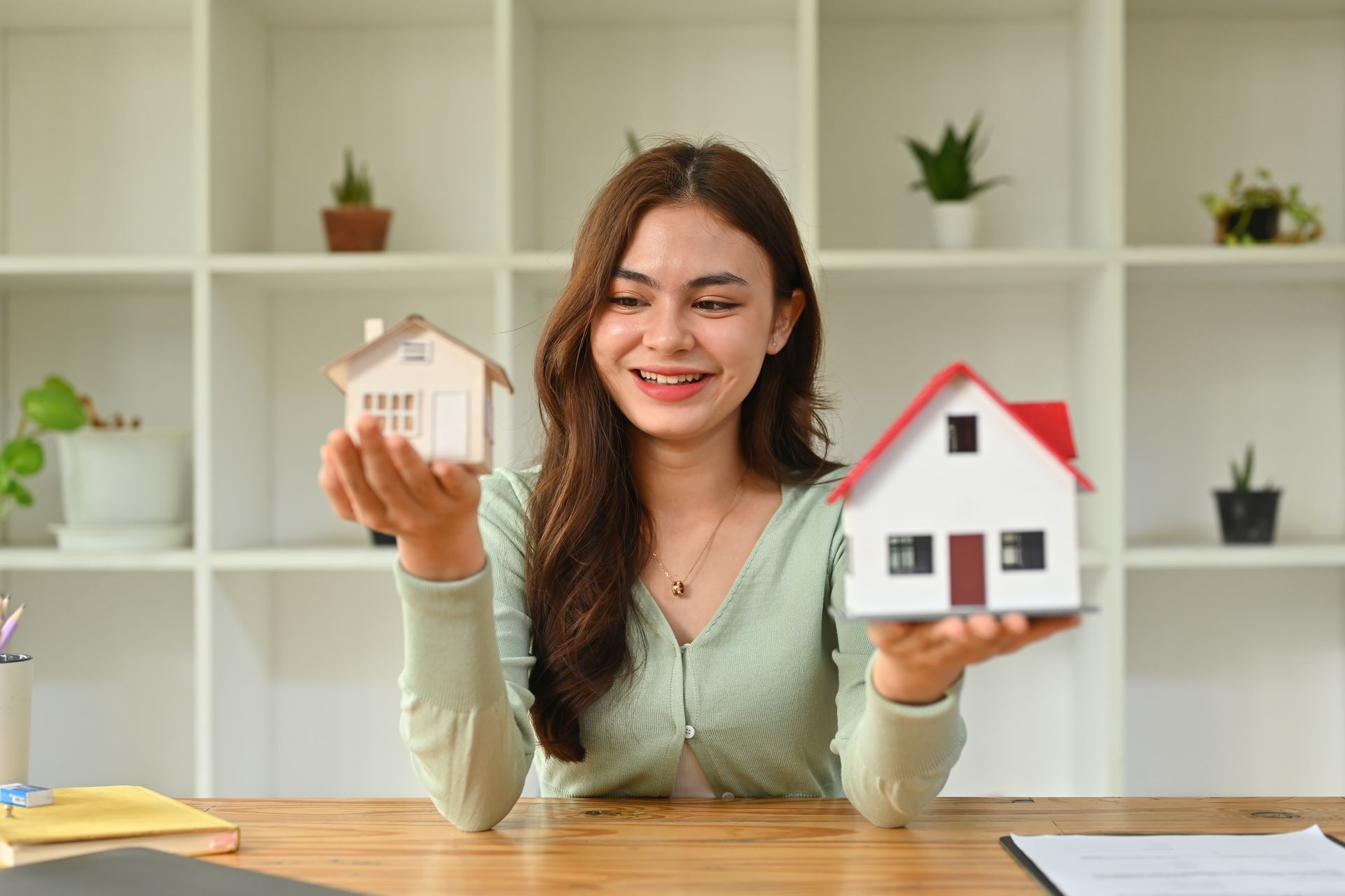 Woman holding model houses, smiling, office setting.