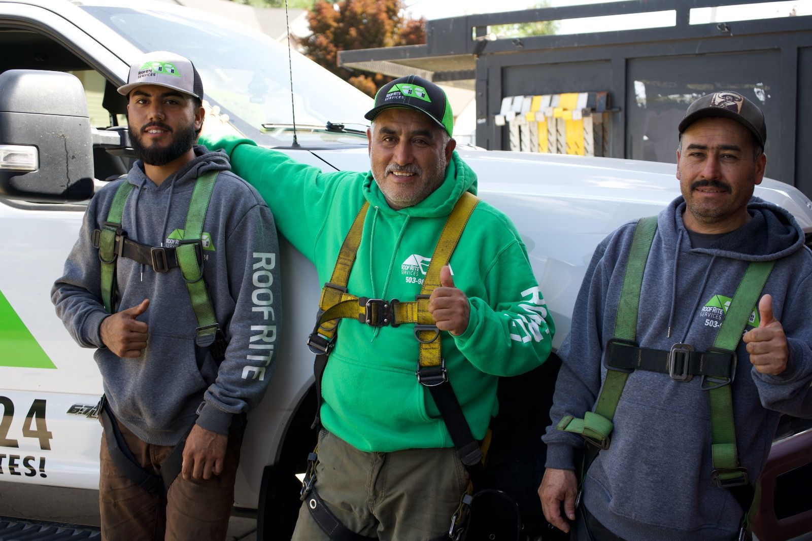 Three men in safety harnesses with thumbs-up in front of a truck, advertising