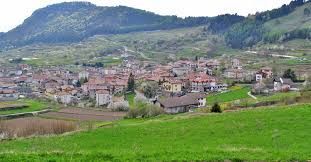 Town nestled at the base of a mountain, with green fields in the foreground.