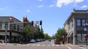 Street scene in downtown with buildings, cars, trees, and a red traffic light under a blue sky.