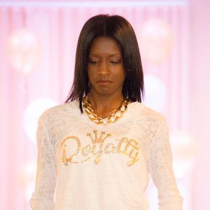 A woman wearing a white sweater and a gold necklace is standing on a runway.