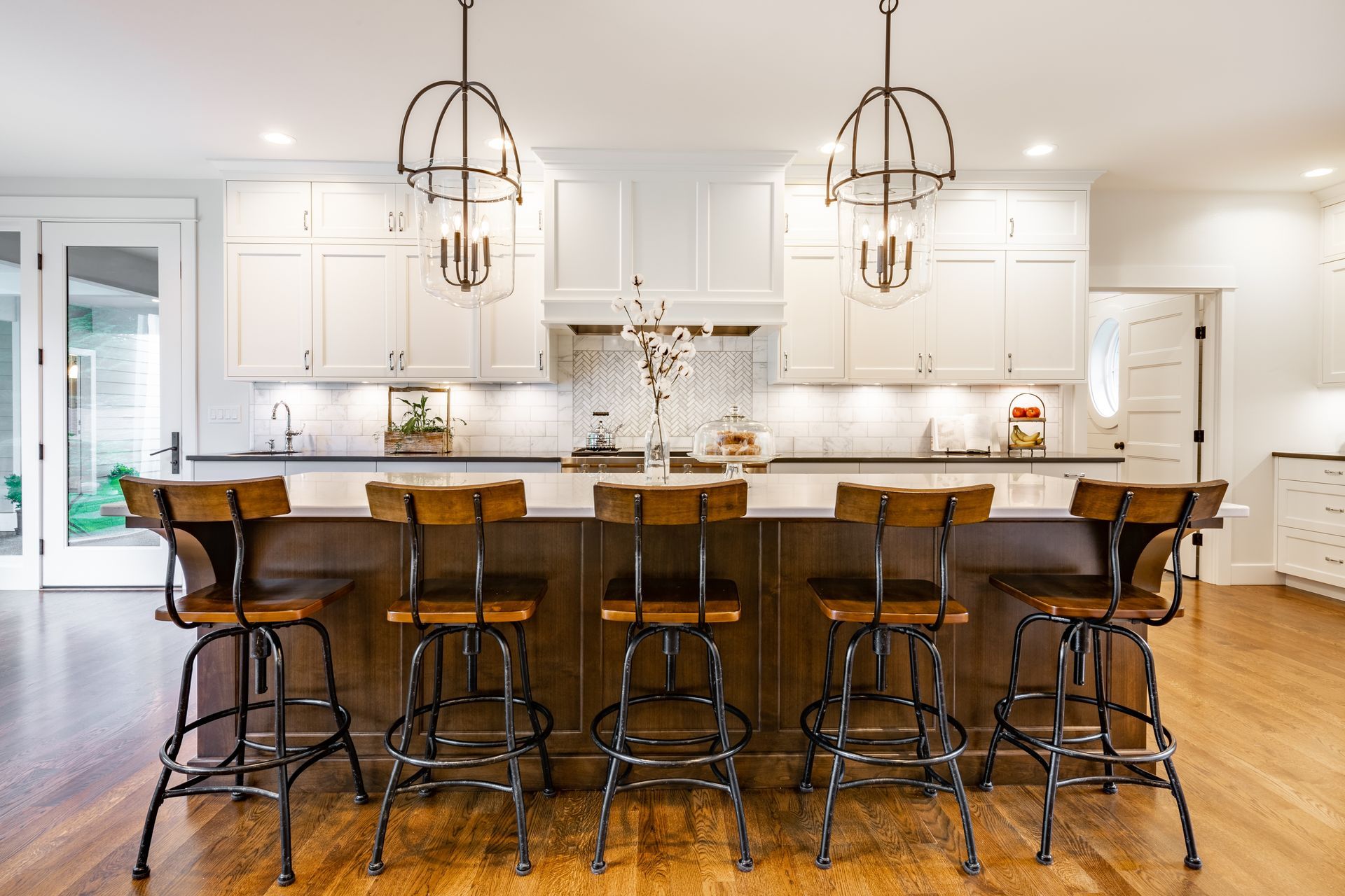 A kitchen with white cabinets and wooden stools and a large island.