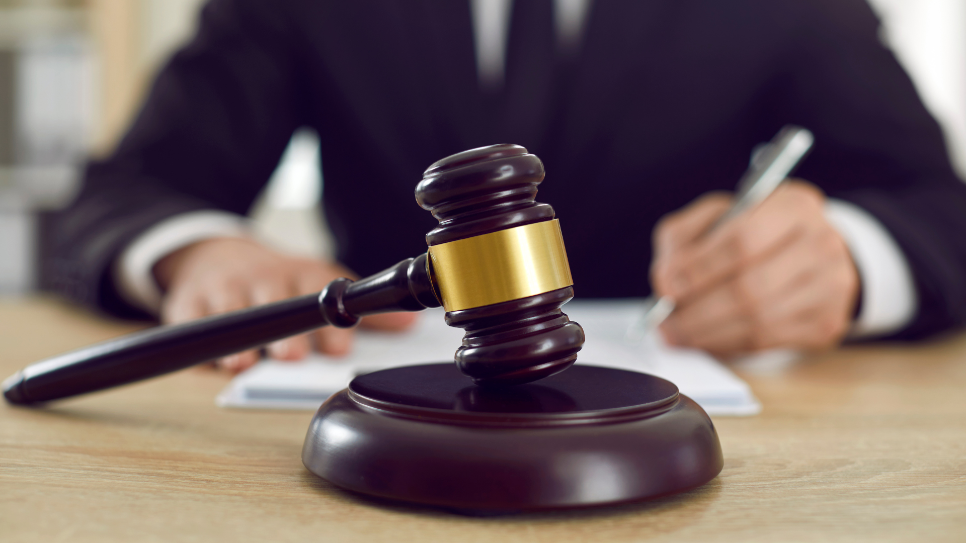 A judge is sitting at a table writing on a piece of paper next to a wooden gavel.
