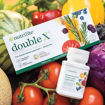 A box of nutrilite double x is surrounded by fruits and vegetables.