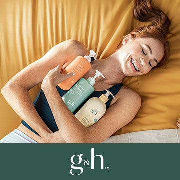 A woman is laying on a bed holding three bottles of shampoo.