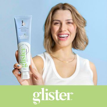 A woman is holding a tube of glister toothpaste.