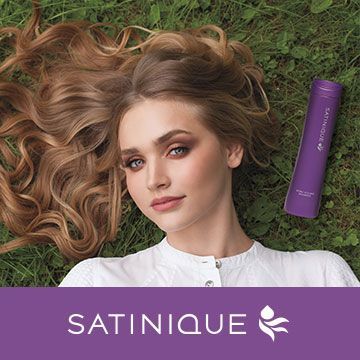 A woman is laying on the grass next to a bottle of satinique shampoo.