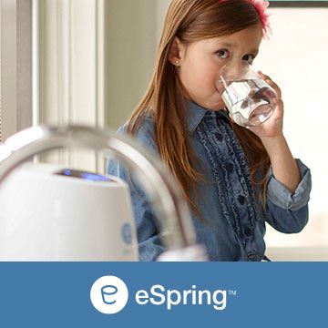 A little girl is drinking water from a glass.