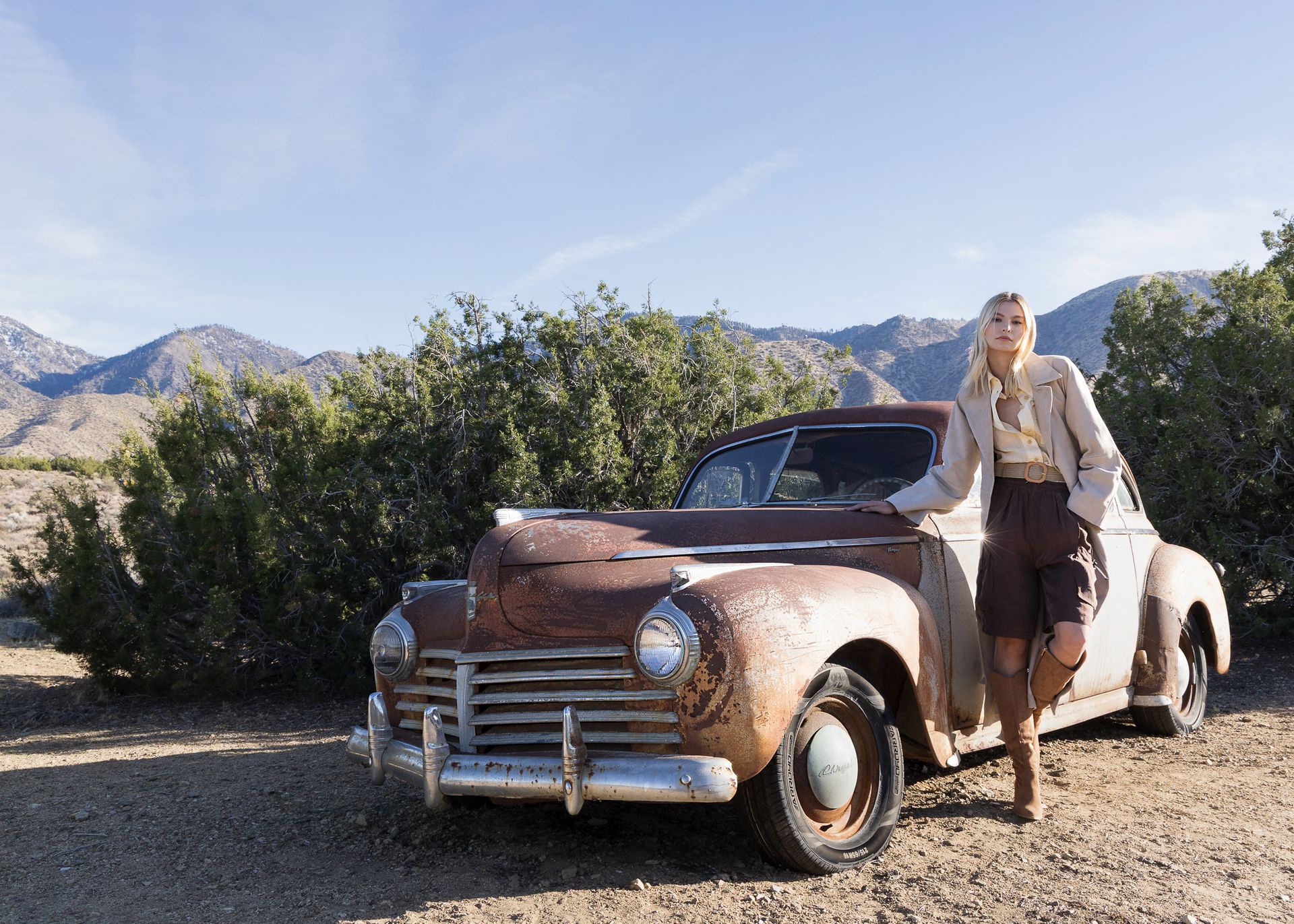A woman is standing next to an old rusty car.