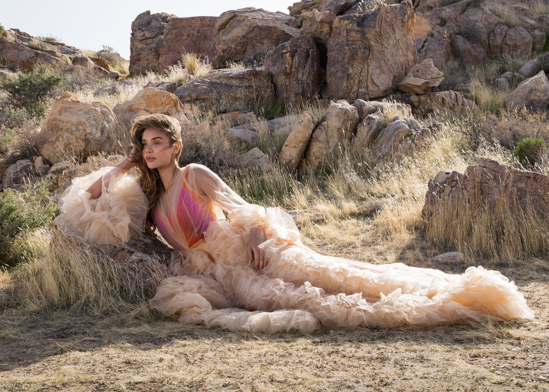 A woman in a long dress is laying on the ground in the desert.