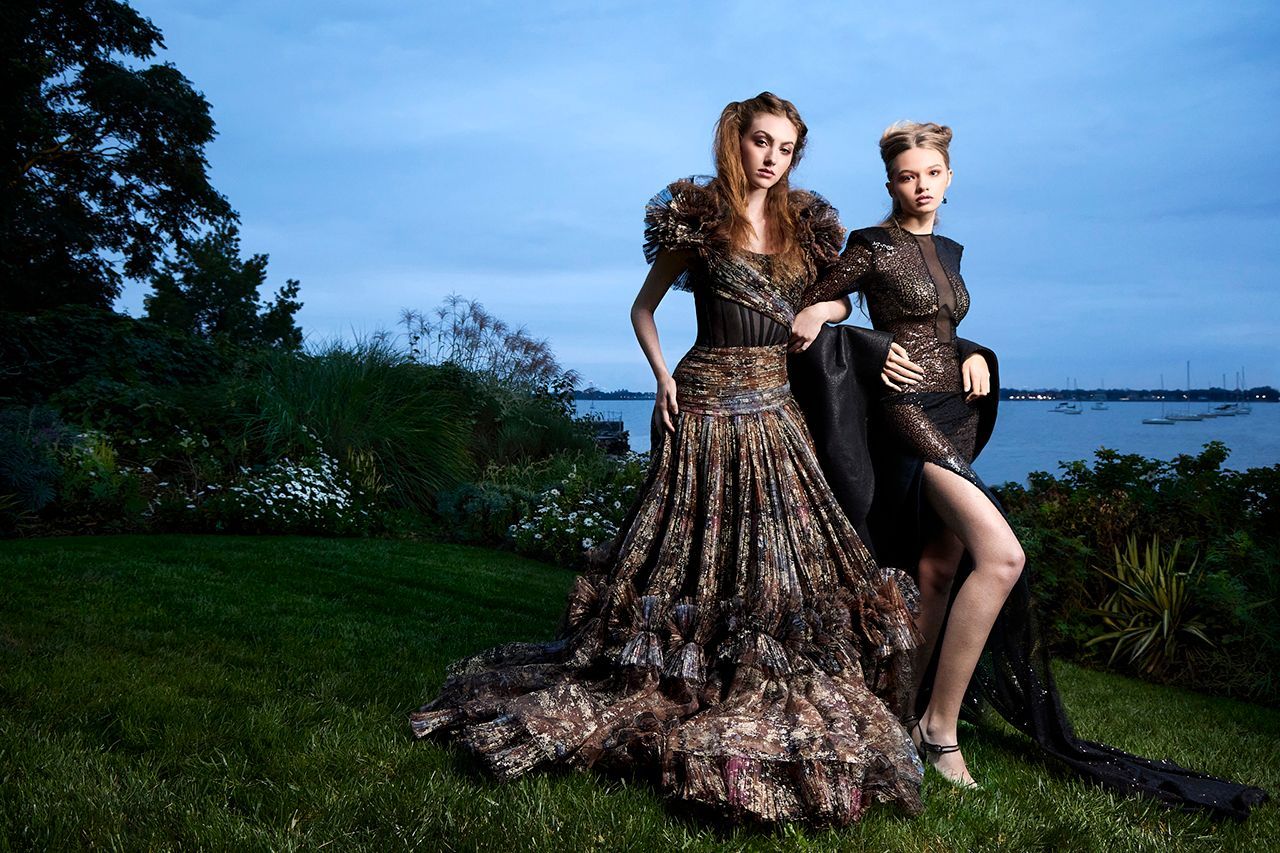 Two women in long dresses are standing next to each other in the grass.