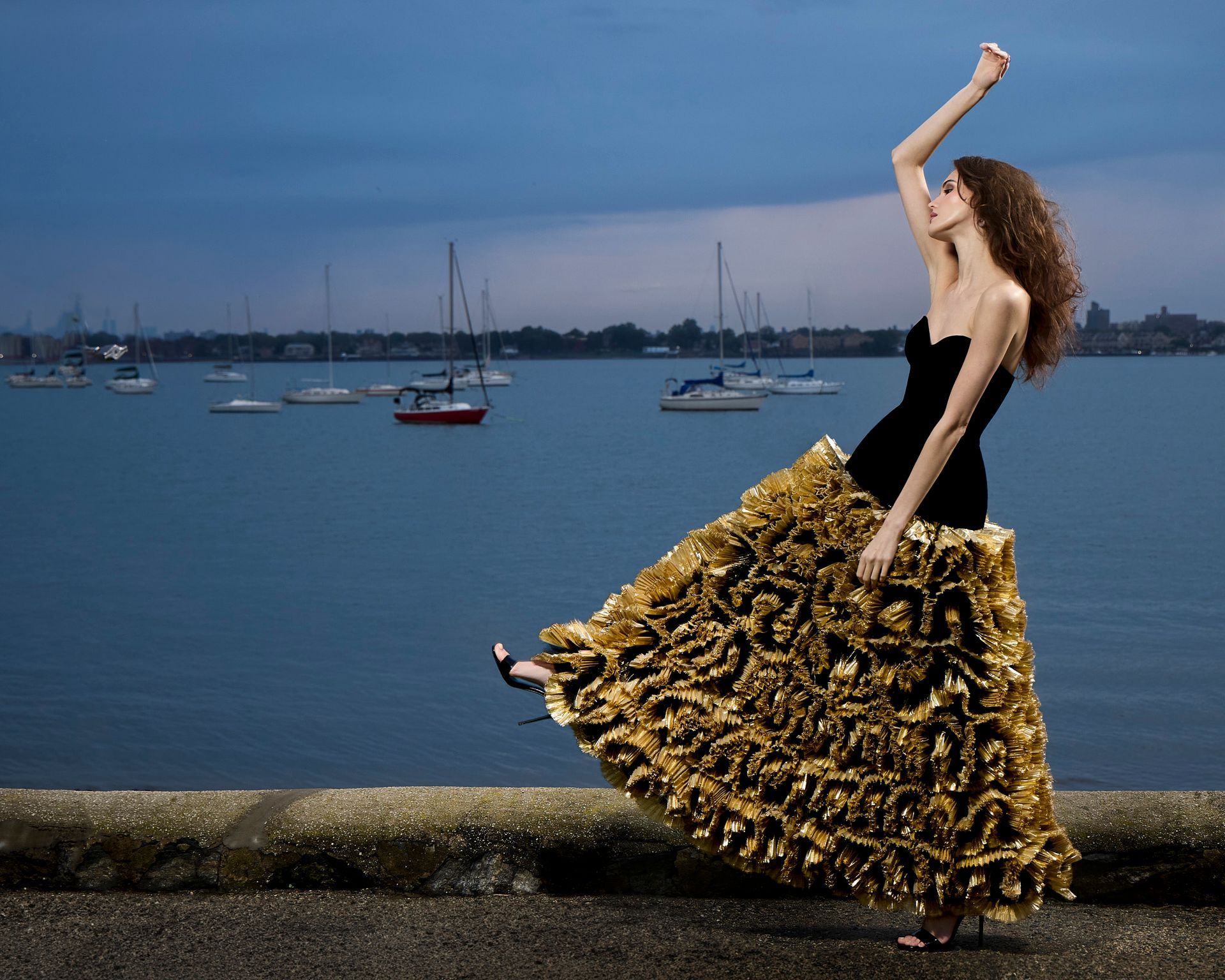International vogue model in high-end evening gown. Standing in the grass near a body of water with high stride.