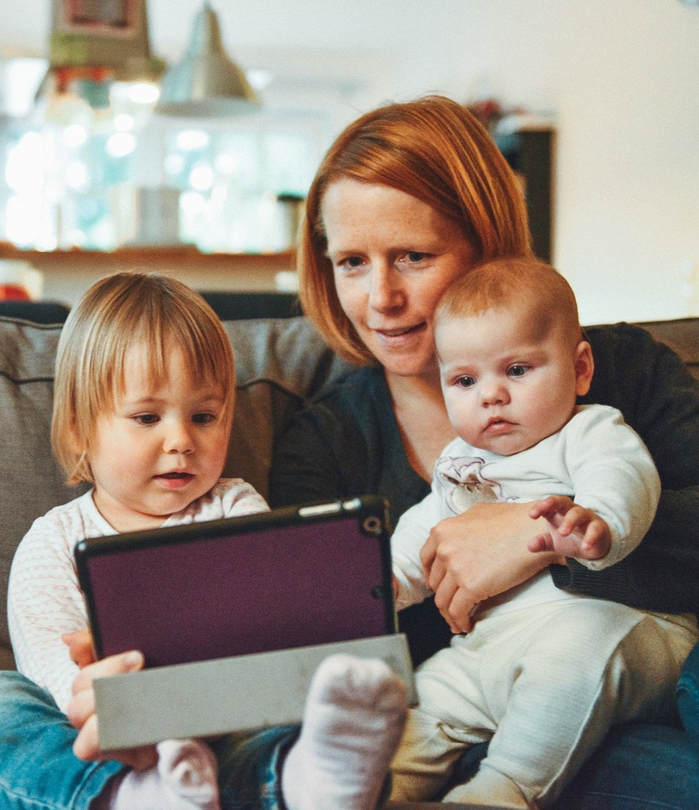 mother playing with tablet with daughter while holding baby