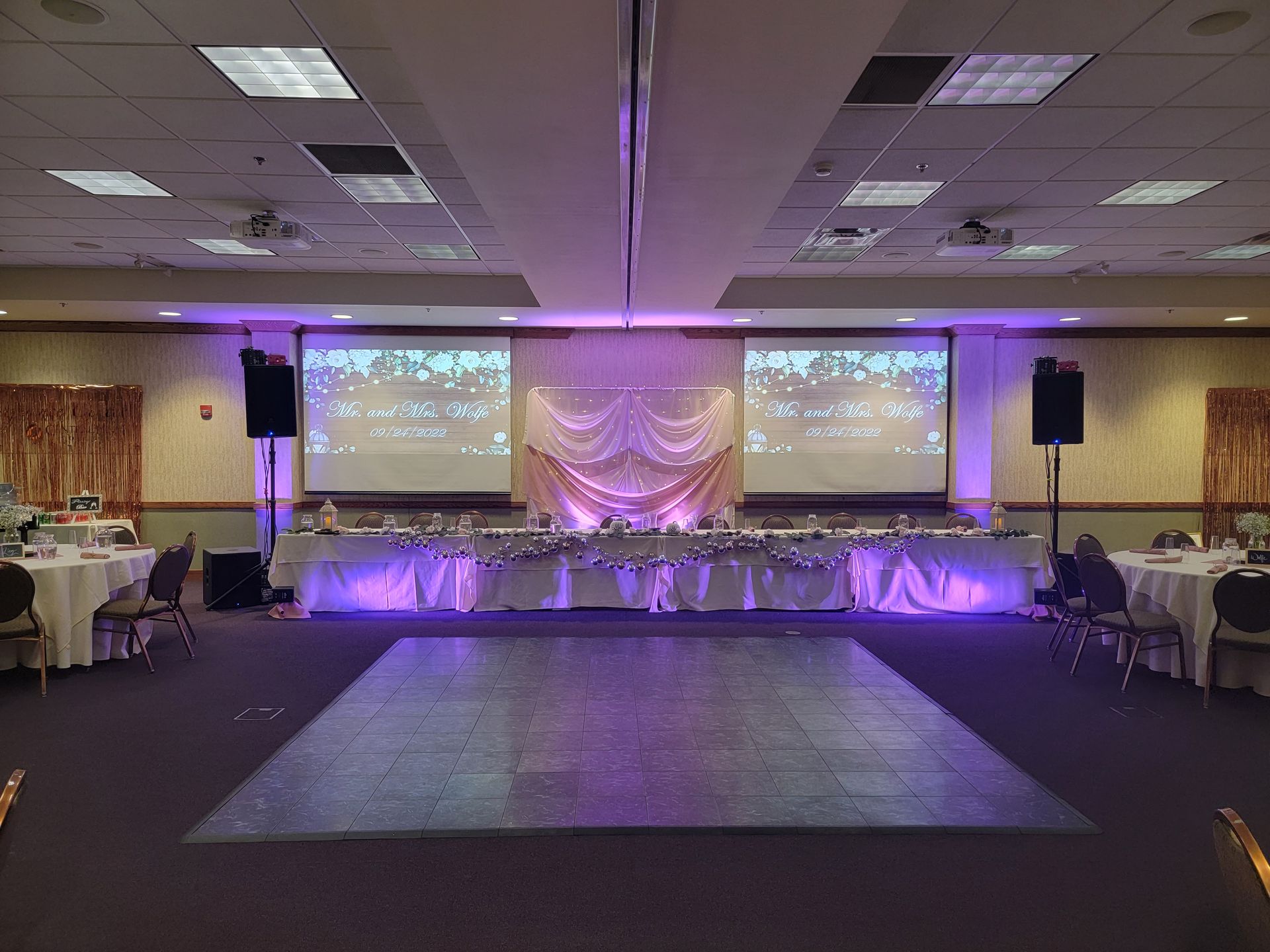 A dimly lit event space featuring a long bar, tables with red tablecloths, seating areas, and hanging globe lighting.