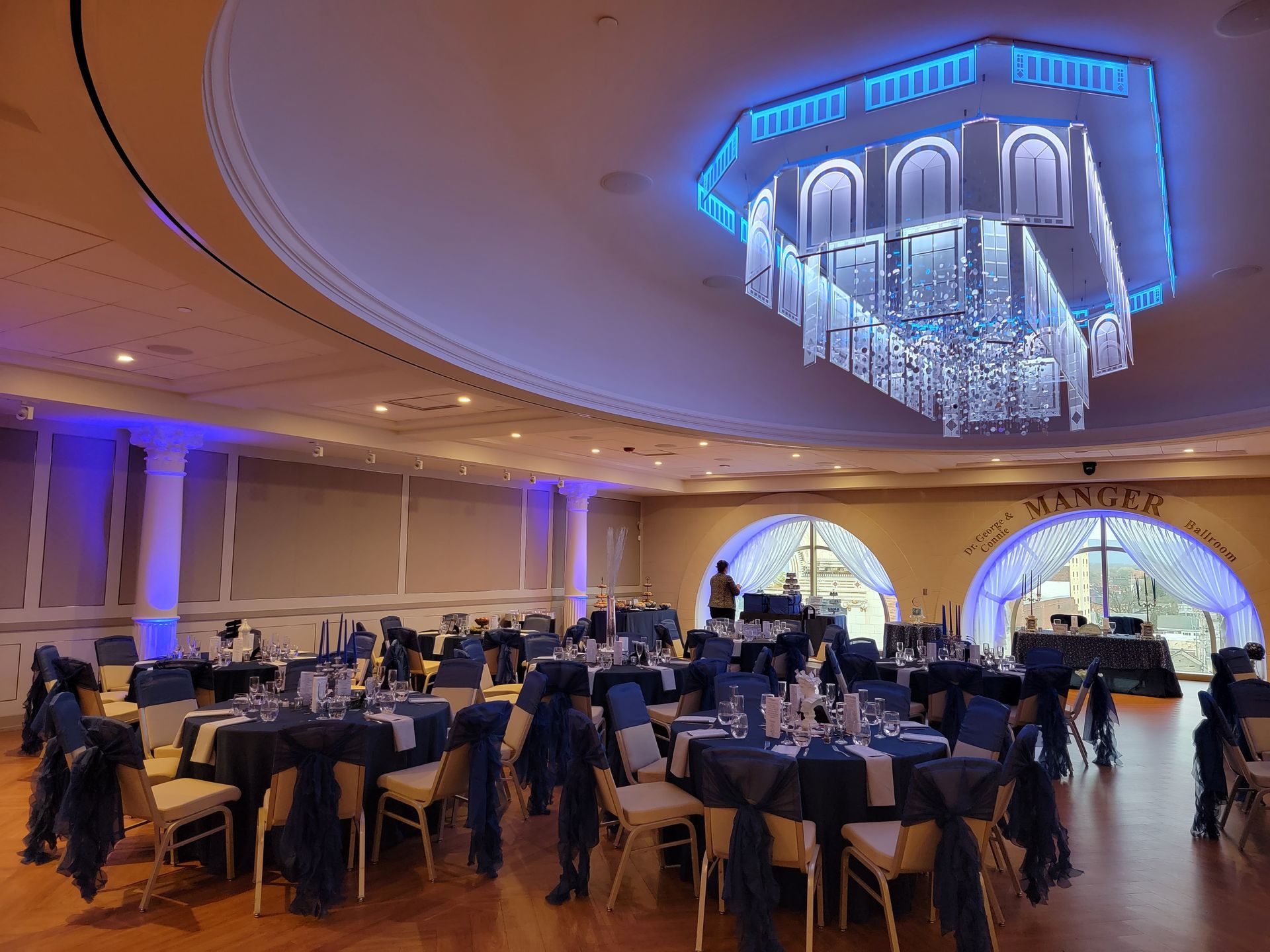 A dimly lit event space featuring a long bar, tables with red tablecloths, seating areas, and hanging globe lighting.