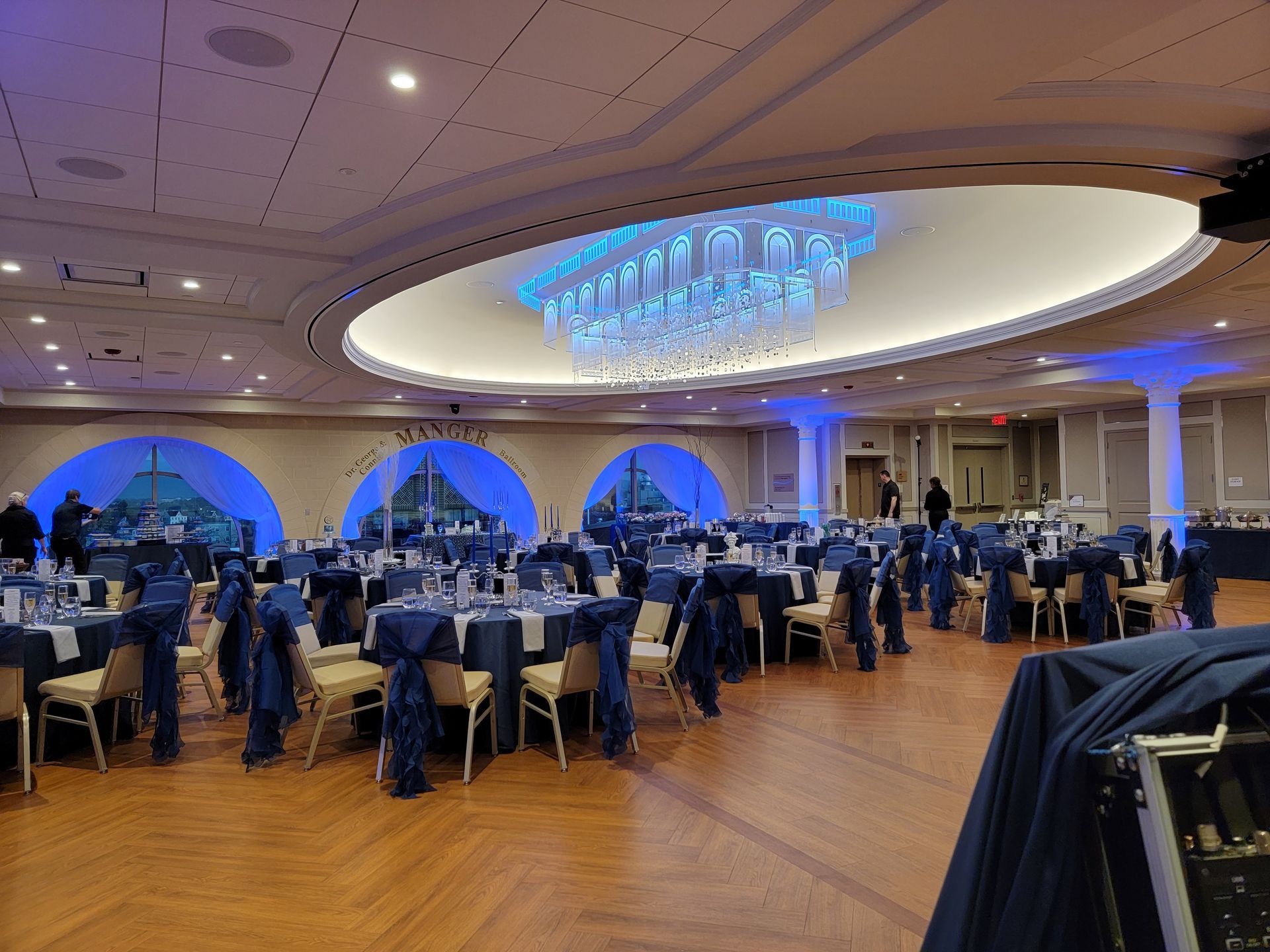 A dimly lit event space featuring a long bar, tables with red tablecloths, seating areas, and hanging globe lighting.