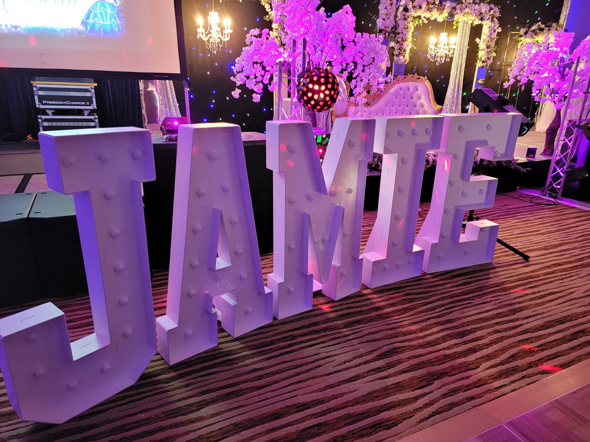 A dimly lit event space featuring a long bar, tables with red tablecloths, seating areas, and hanging globe lighting.
