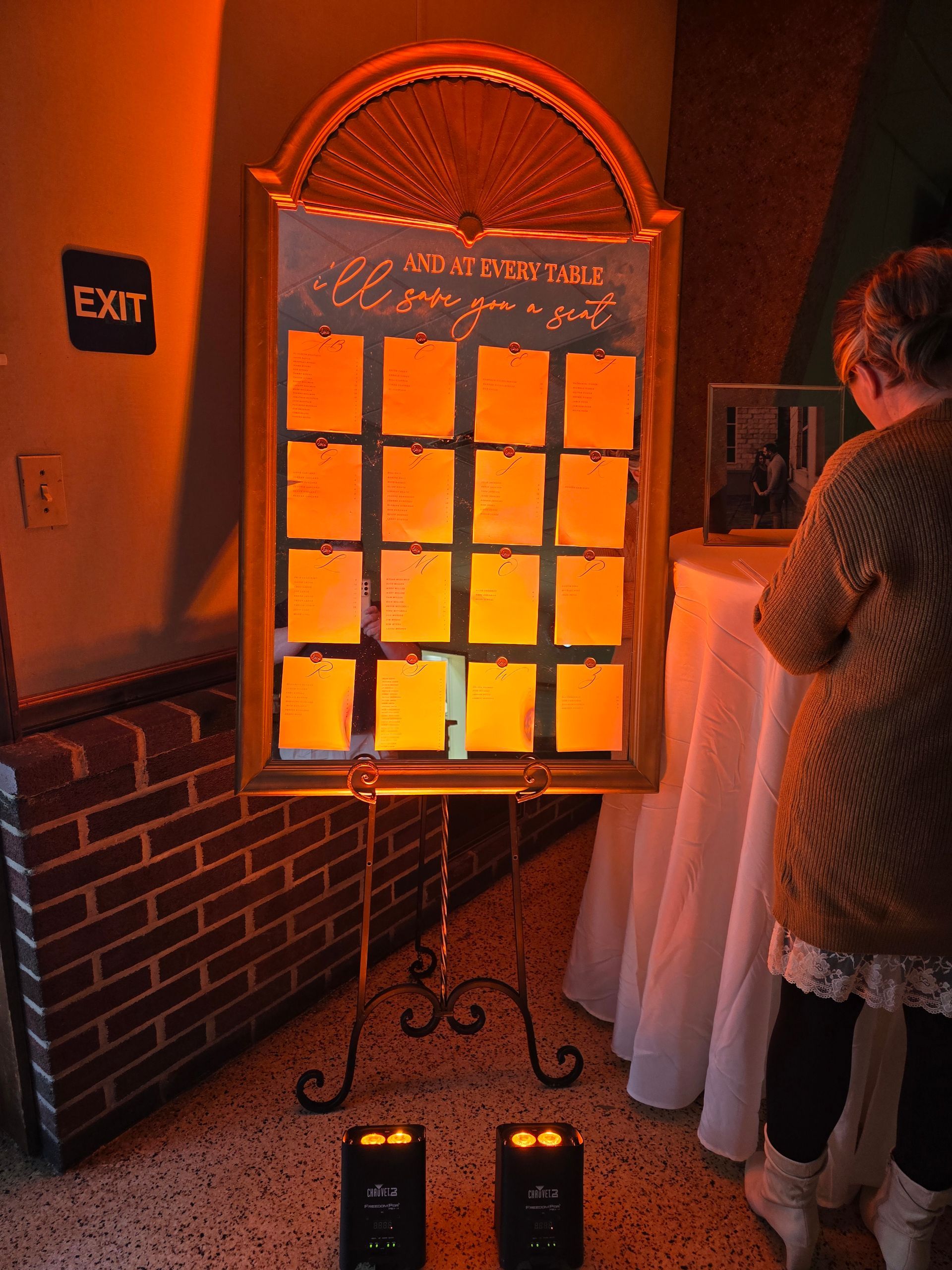 A dimly lit event space featuring a long bar, tables with red tablecloths, seating areas, and hanging globe lighting.