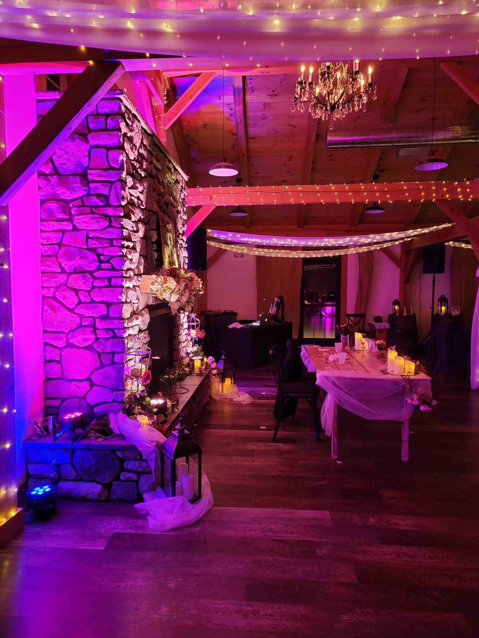 A rustic venue interior with a stone fireplace, ambient pink lighting, string lights, and tables set for an event.