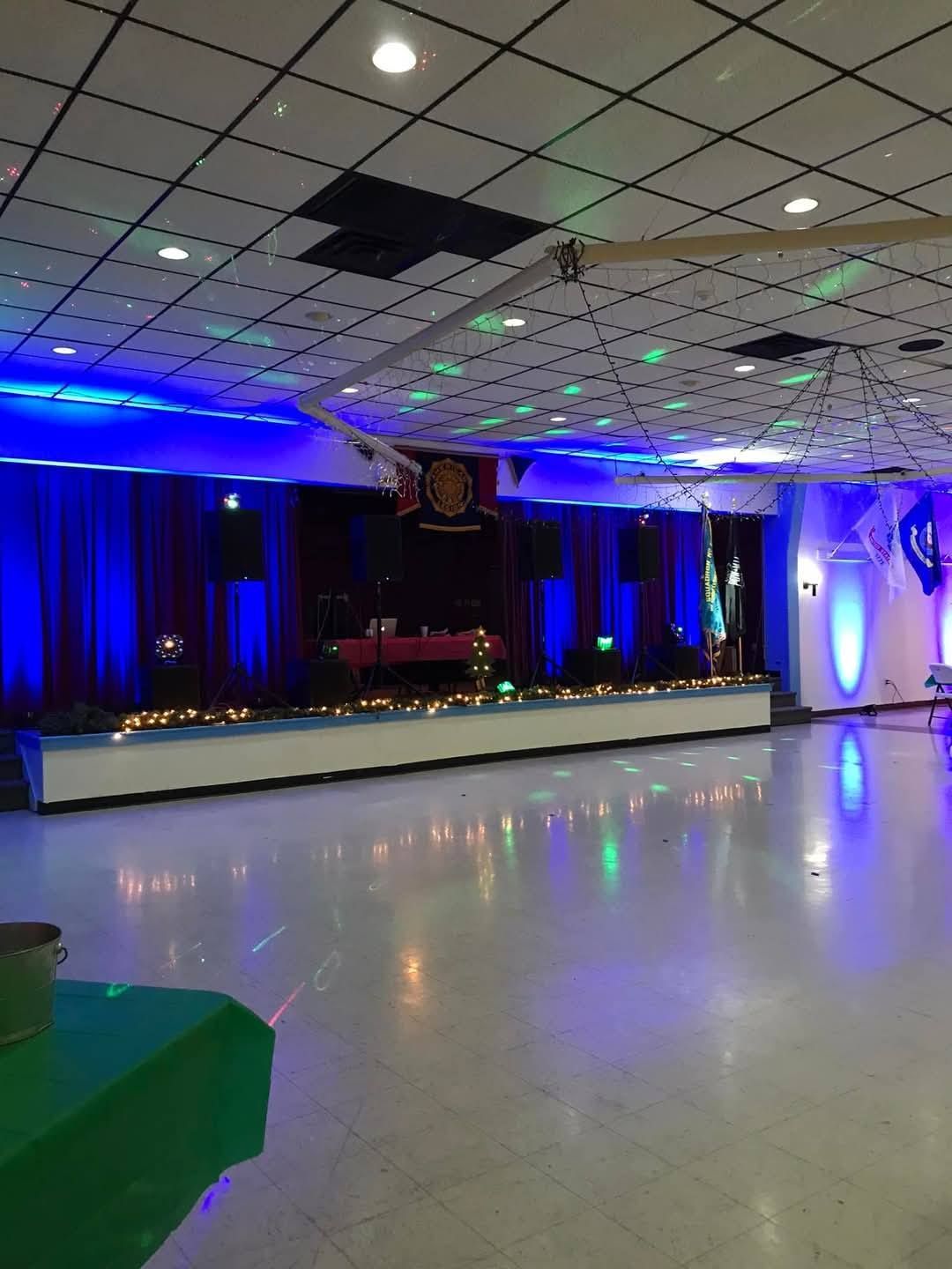 An empty event hall with a raised stage, blue mood lighting, and patterned ceiling tiles.