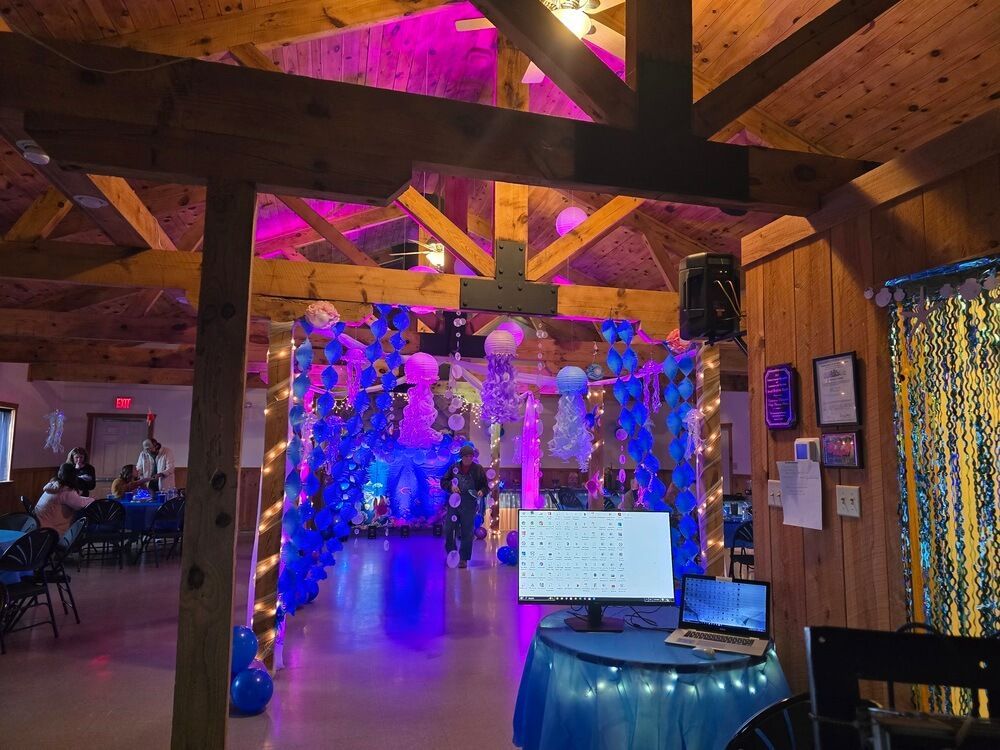 An indoor event space decorated with blue and purple balloon arches and soft lighting, with a computer monitor on a desk.