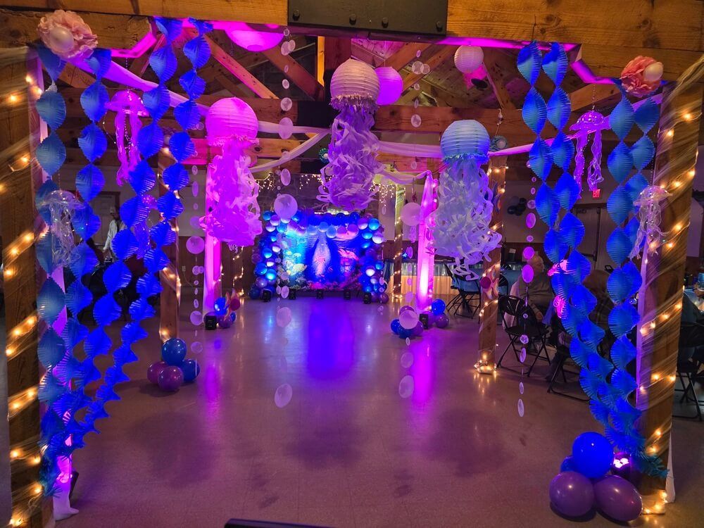 A room decorated for an underwater-themed party with blue paper garlands, jellyfish lanterns, and purple ambient lighting.