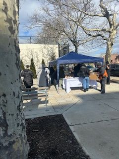 A blue tent set up outdoors with people gathered around tables, possibly a market or distribution event.