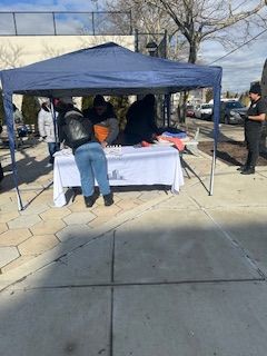 People at a table under a blue canopy outside. One person is writing.