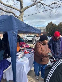 A street market with people browsing items under a blue tent on a cloudy day.