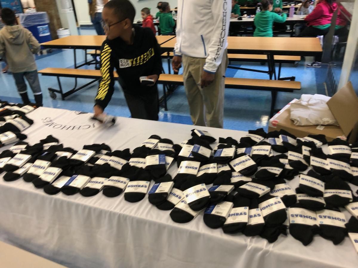 A table filled with lots of black socks and a boy wearing a sweatshirt that says united