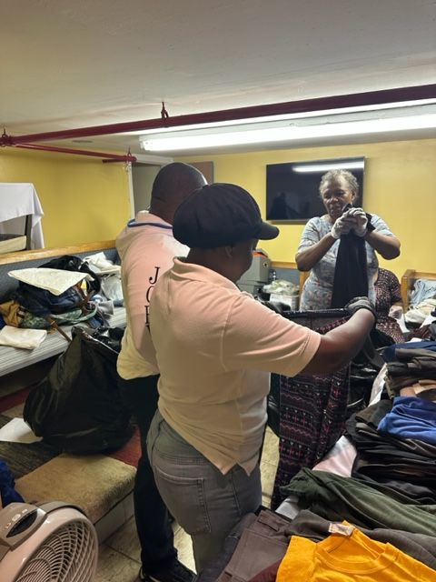 A man and a woman are standing in a room full of clothes.