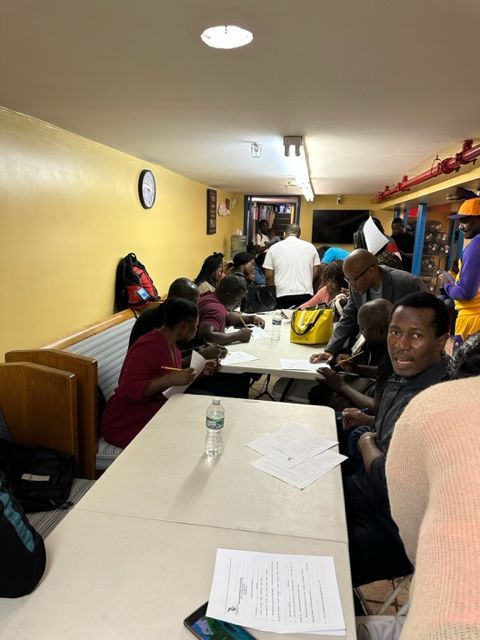 A group of people are sitting at tables in a room with a clock on the wall