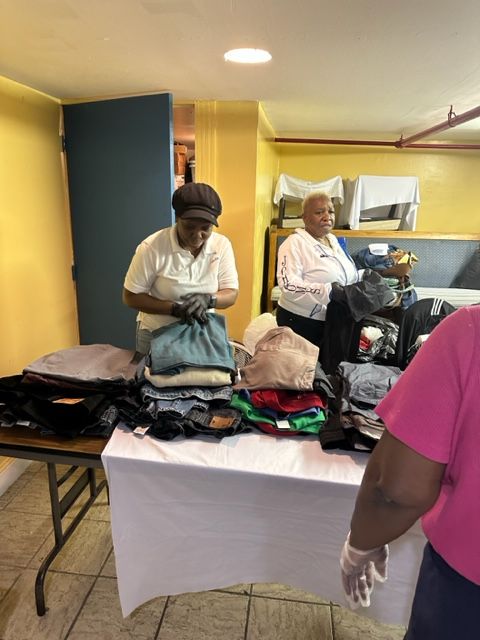 A woman in a pink shirt is standing next to a table with clothes on it.