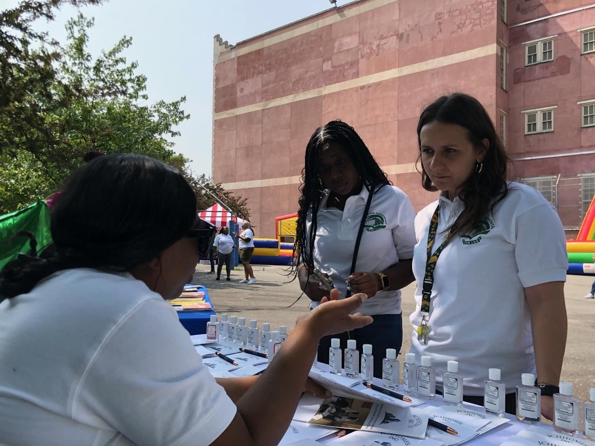 Three women are standing around a table with bottles of hand sanitizer on it.
