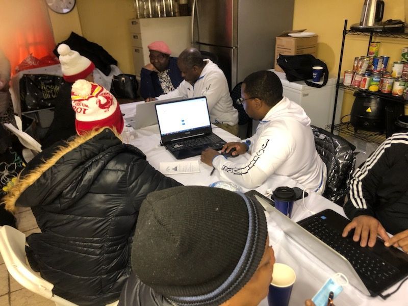 A group of people are sitting around a table with laptops