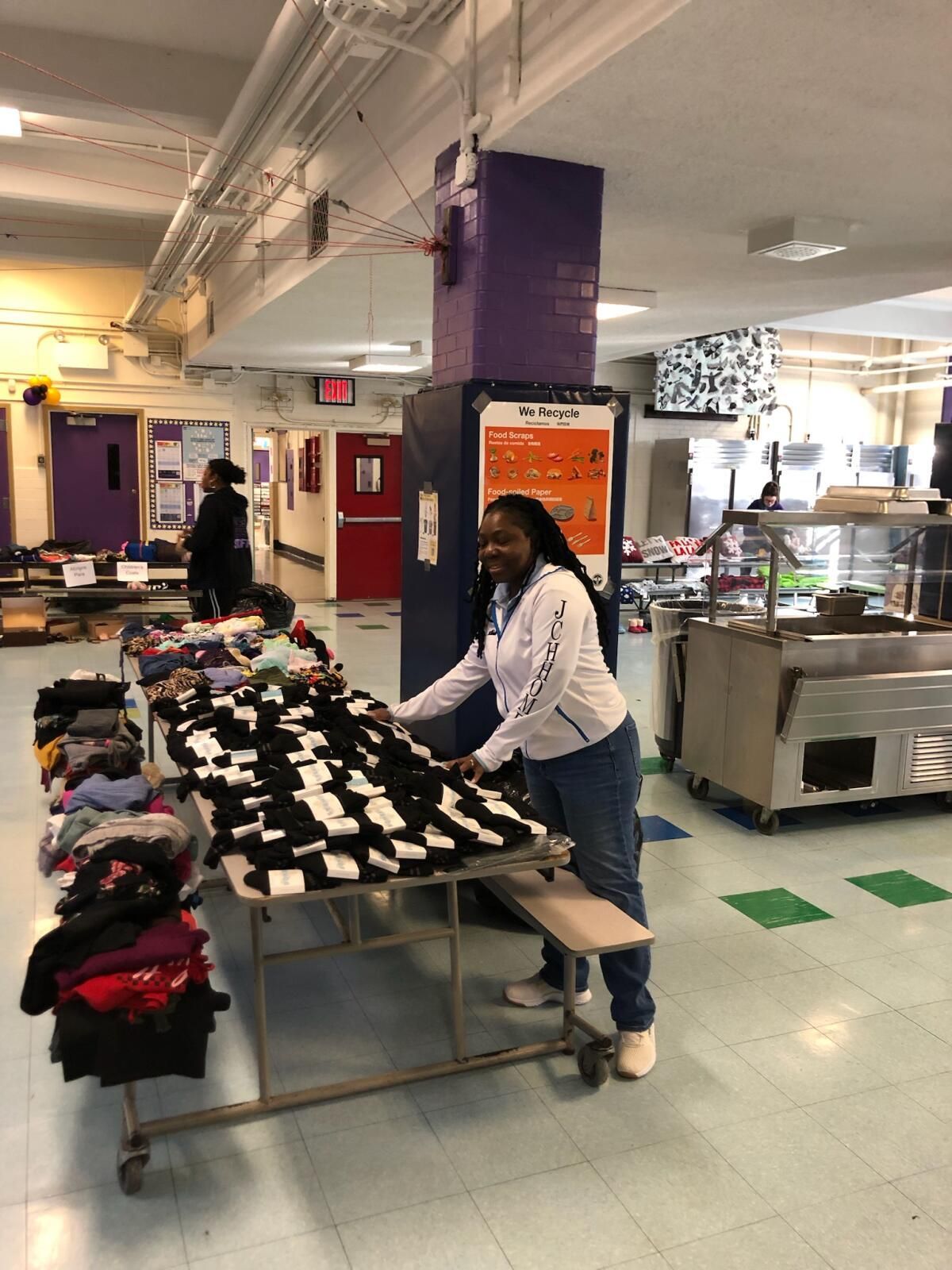 A woman is standing next to a table with a bunch of clothes on it.