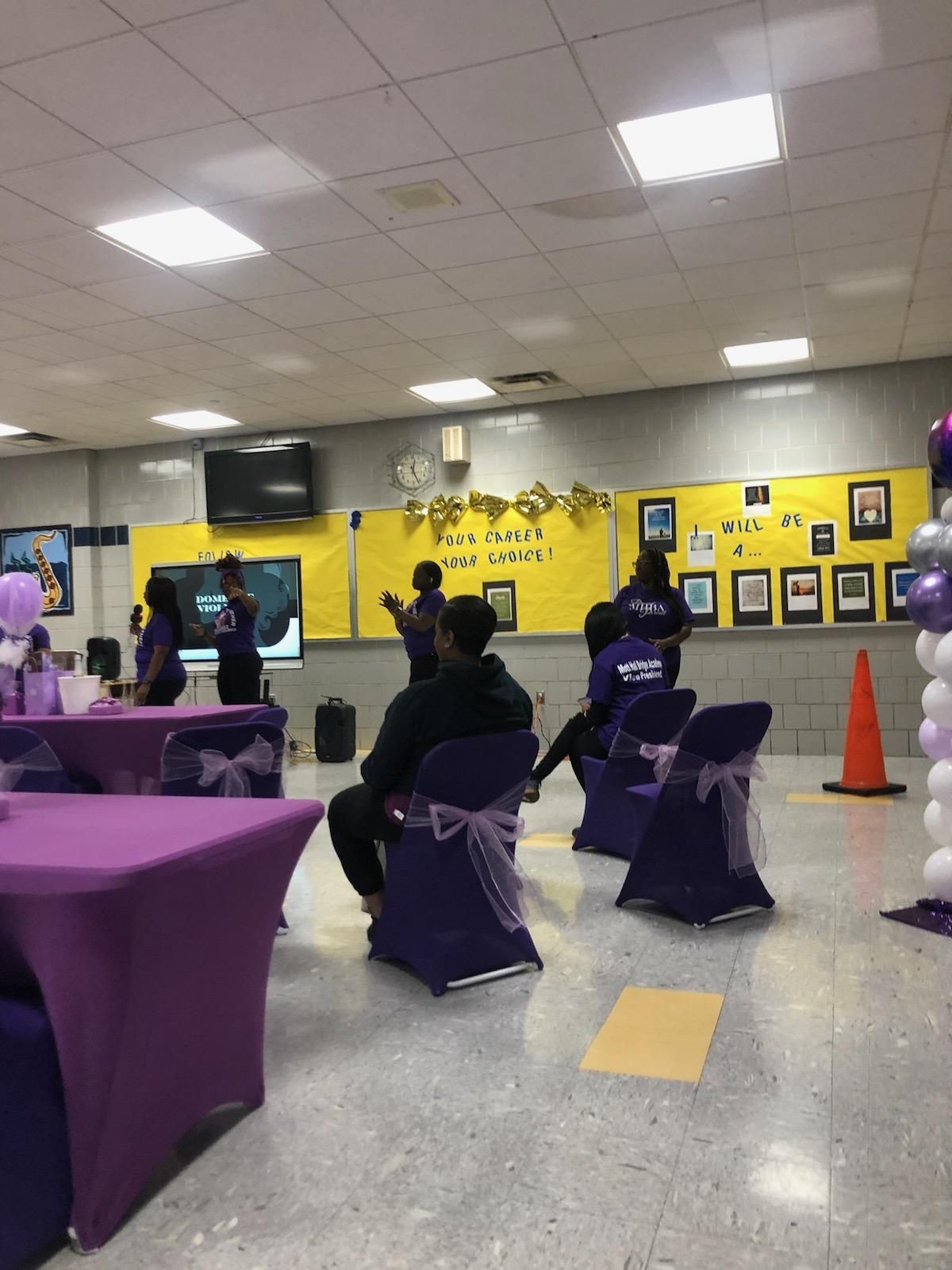 A group of people are sitting in purple chairs in a room.