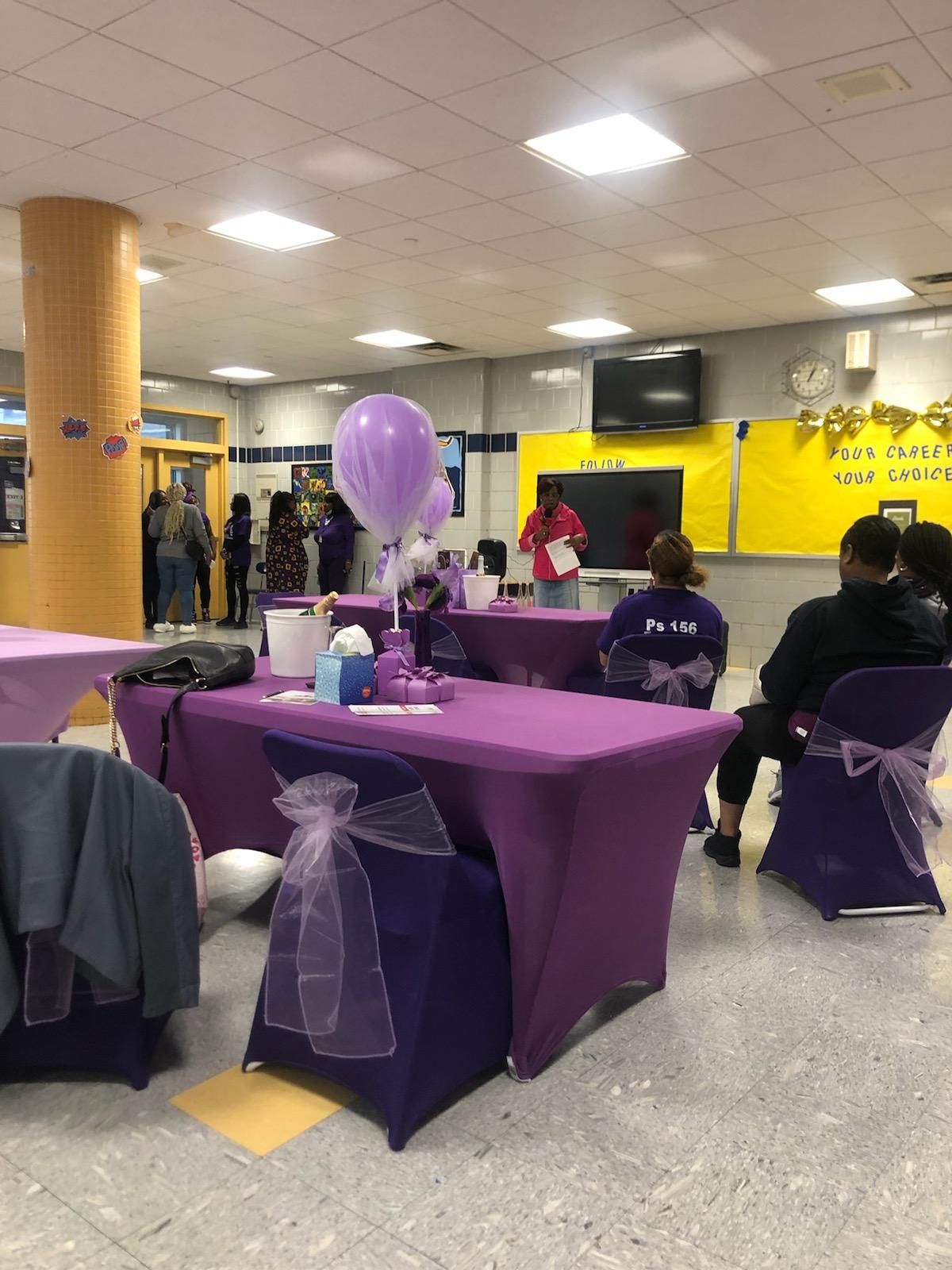 A room with purple tables and chairs and purple balloons.