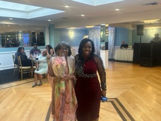 Two women are standing next to each other on a wooden floor in a room.