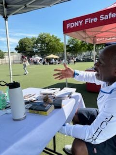 A man is sitting at a table under a tent that says fdny fire safe