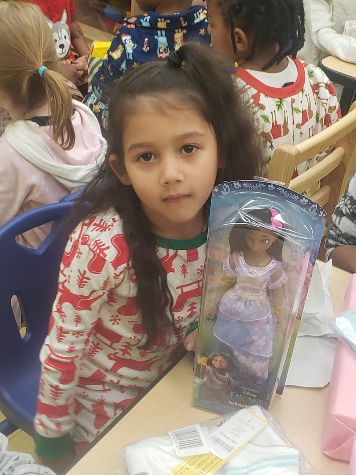 A little girl is sitting at a table holding a doll
