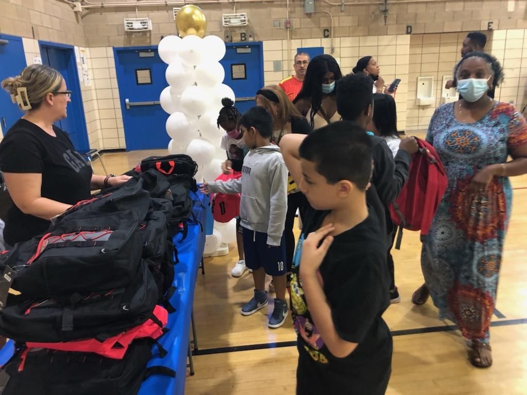 A group of people are standing around a table with backpacks in a gym.