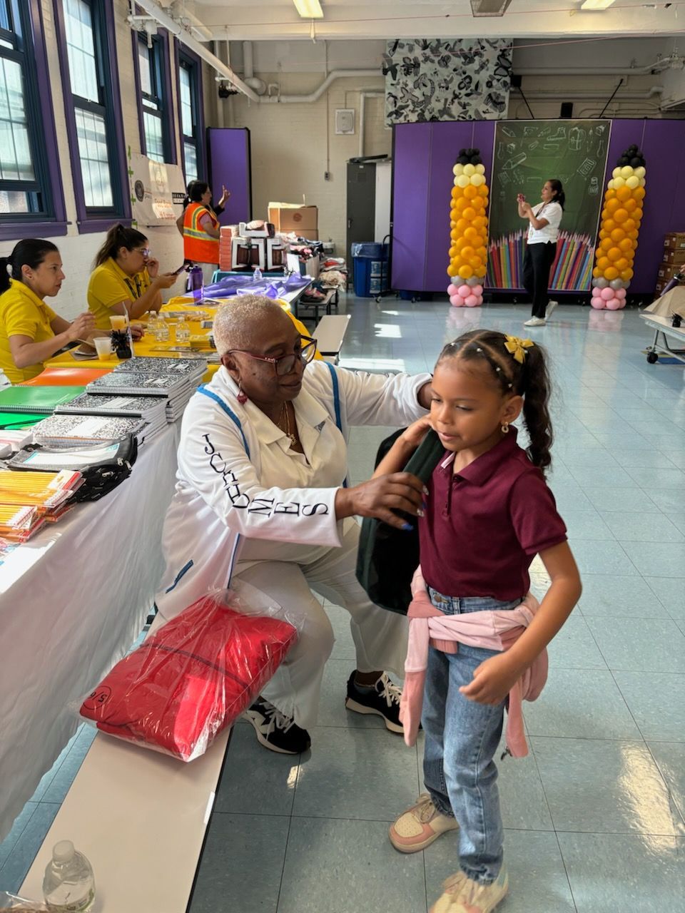A woman is helping a little girl with her backpack in a room.