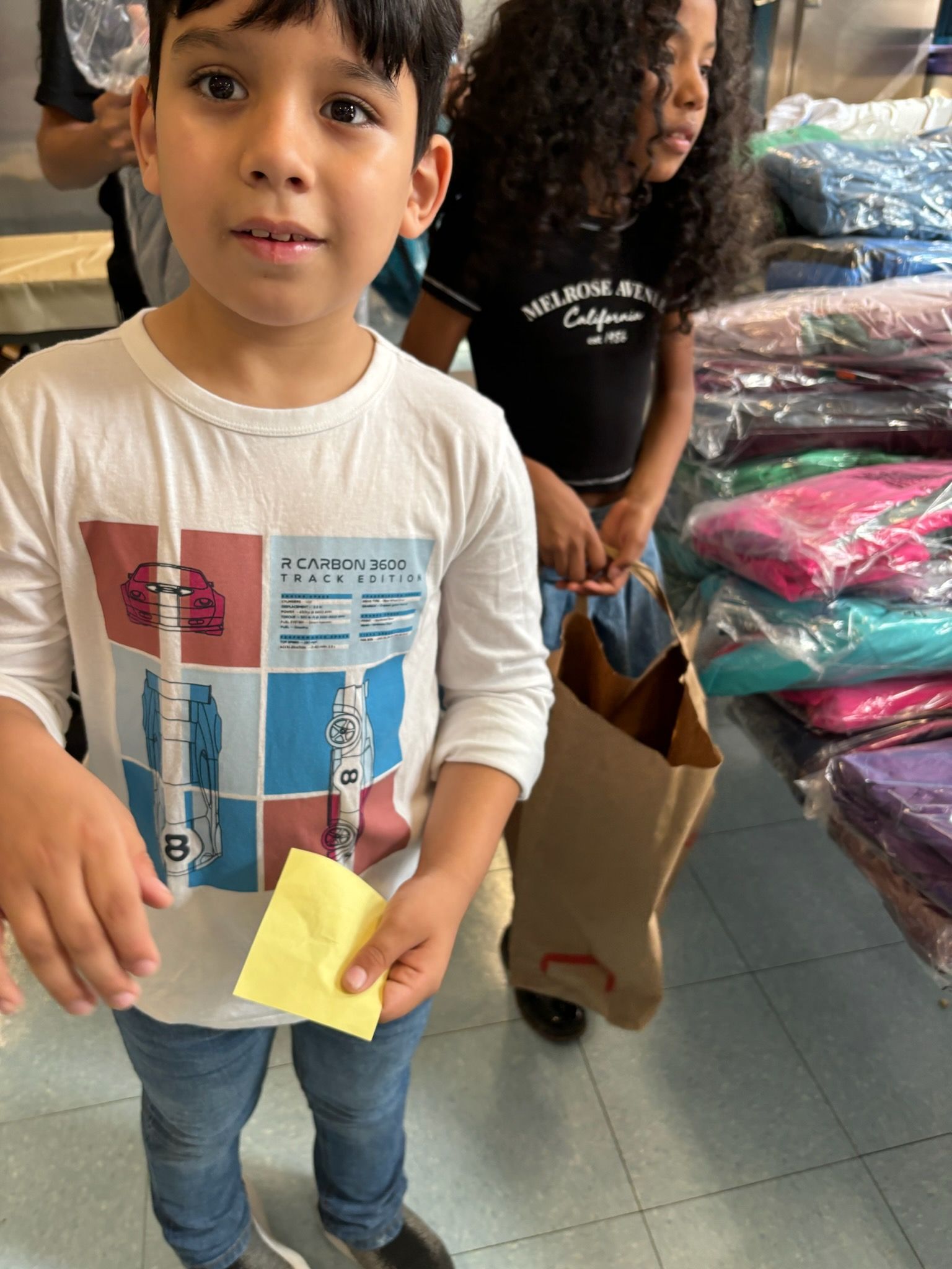 A young boy is holding a piece of paper in front of a pile of clothes.