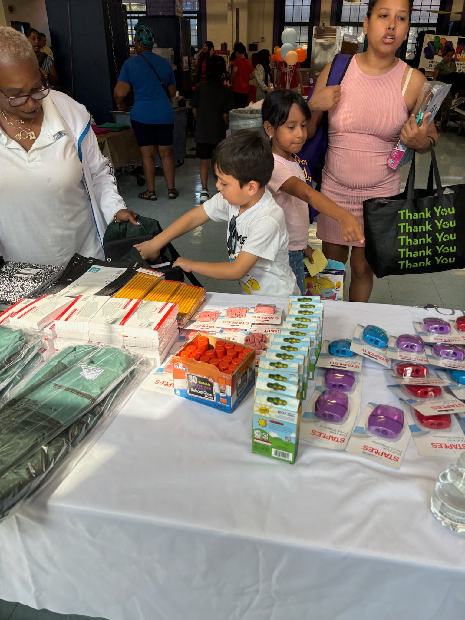 A group of people are standing around a table with a lot of items on it.