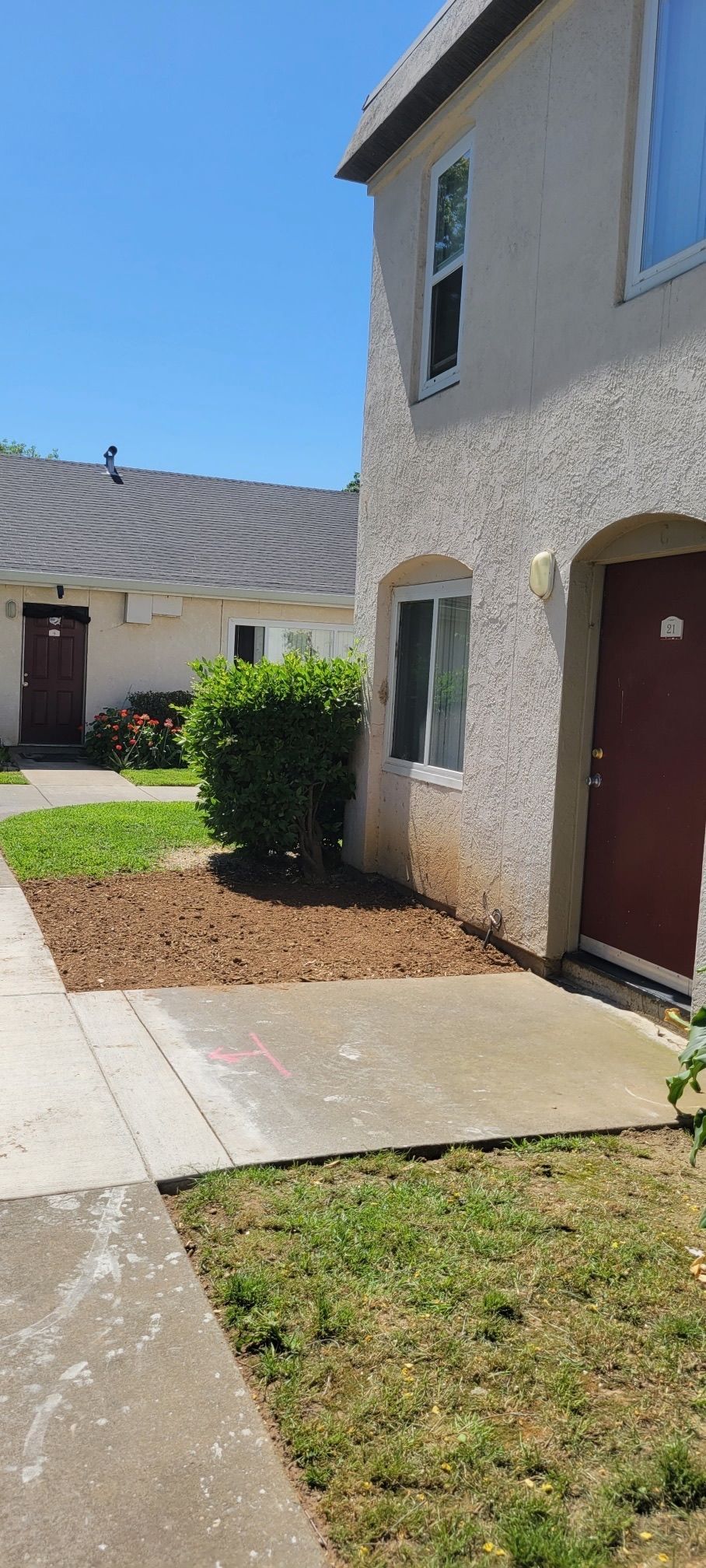 Two-story buildings with red doors, a sidewalk and grass on a sunny day.